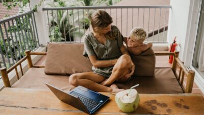 A mother and son relaxing on a balcony with a laptop and coconut nearby.